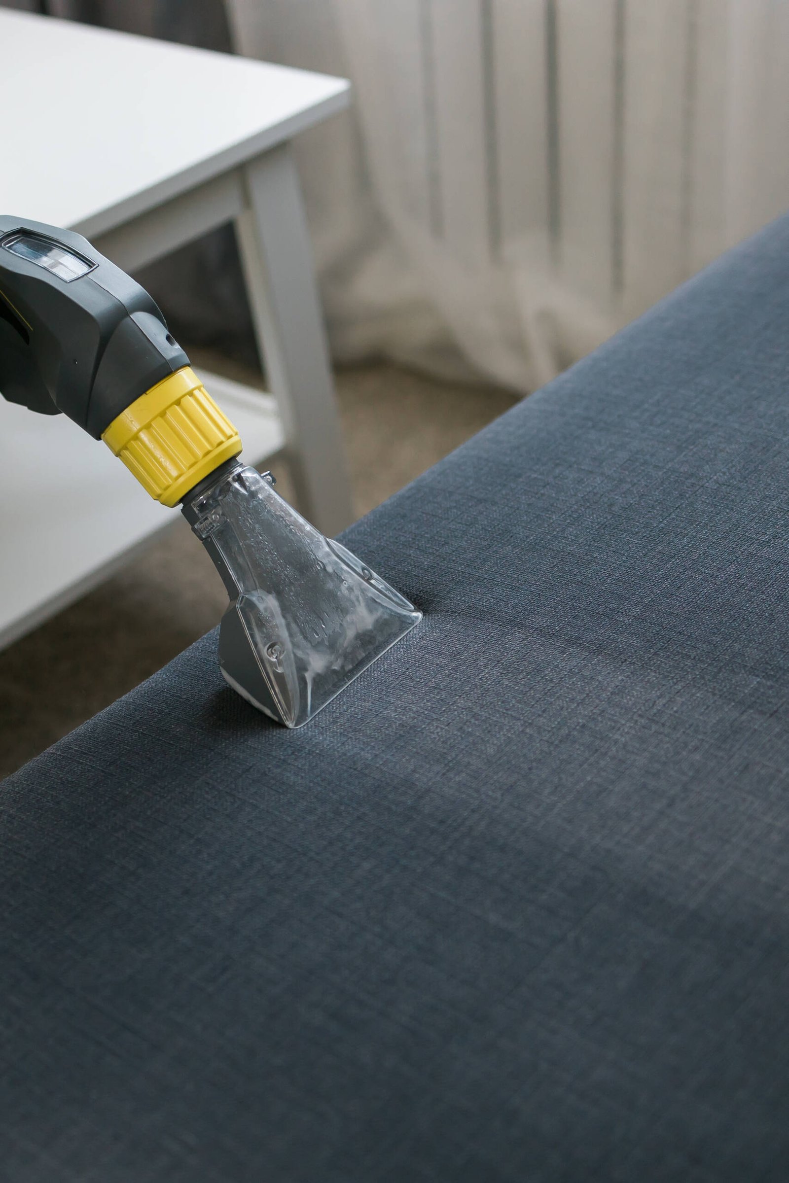 Cleaning service company employee removing dirt from furniture in flat with professional equipment. Man arm cleaning sofa with washing vacuum cleaner
