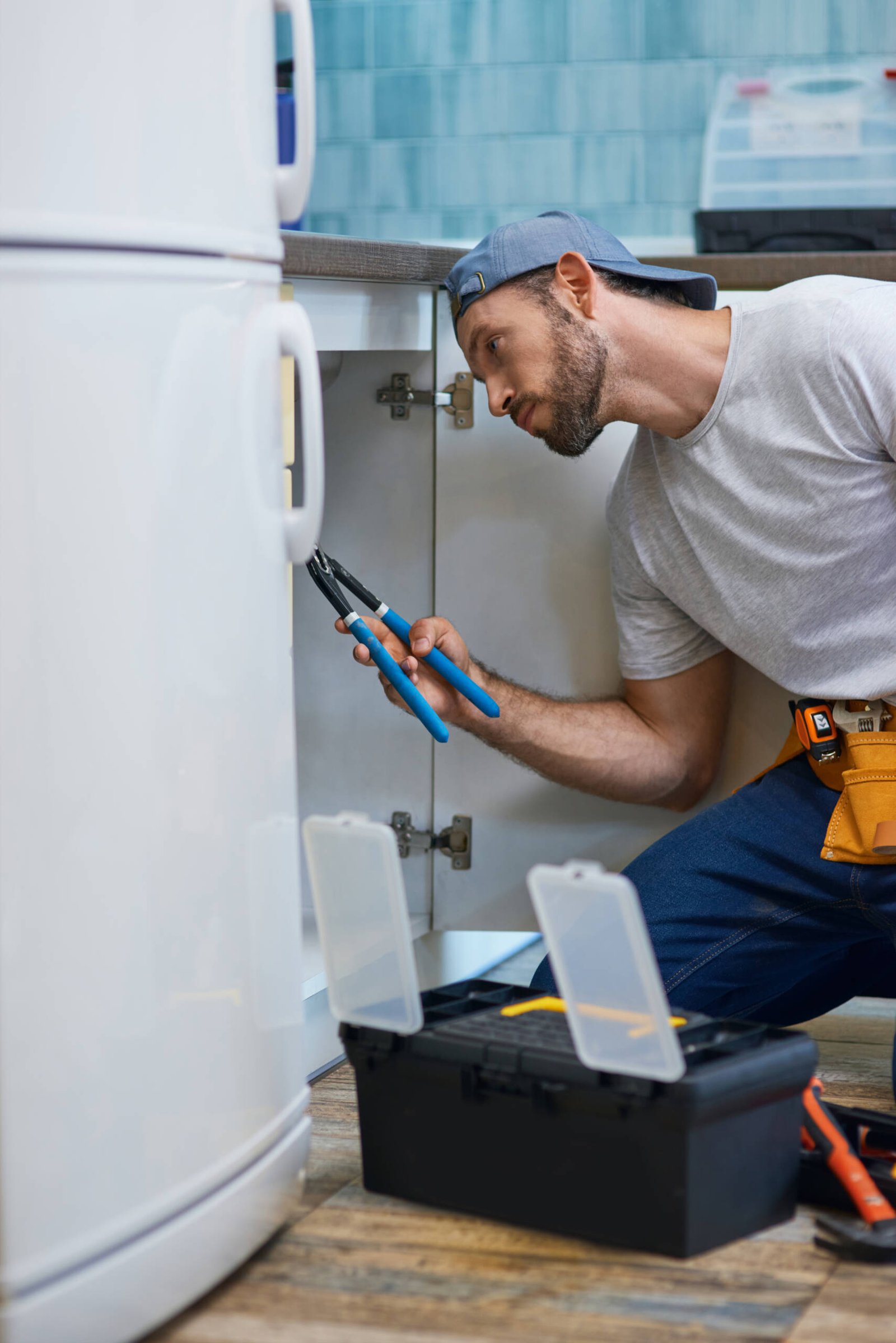 Professional repairman looking focused, using pipe wrench while examining and fixing sink pipe in the kitchen. Repair service and plumbing concept. Side view. Vertical shot