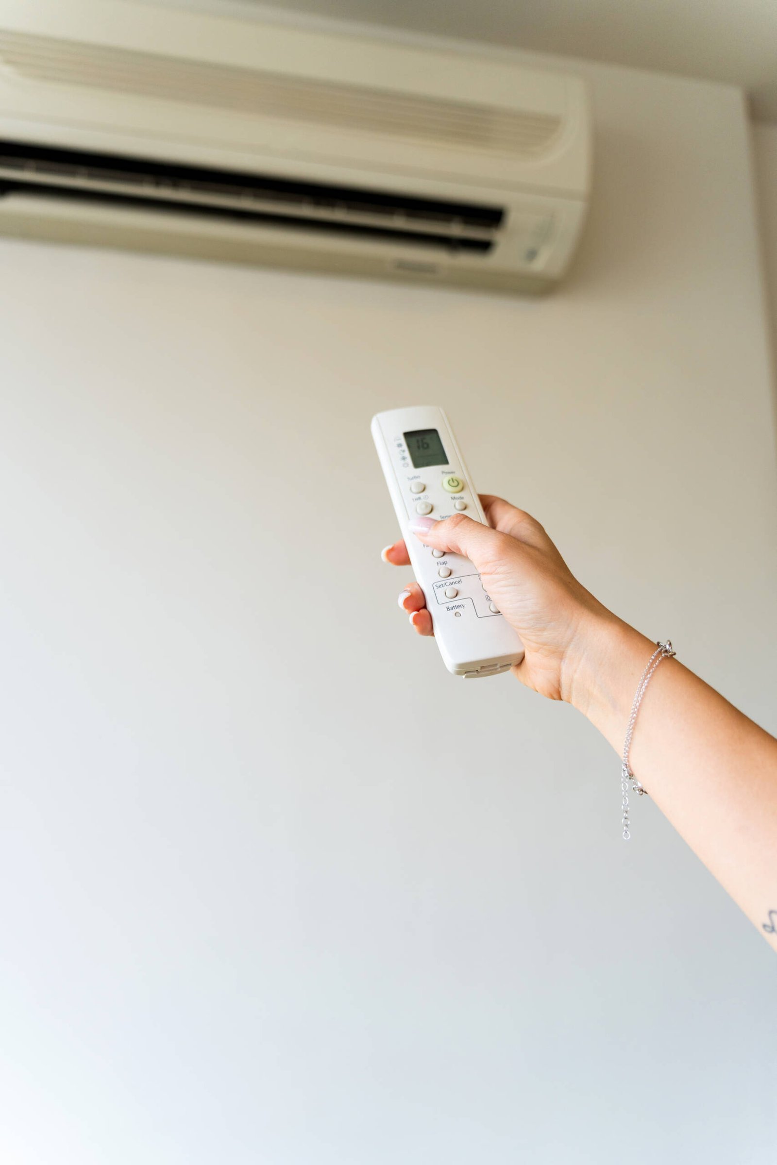 Hand holding a remote control, adjusting temperature settings on an air conditioner, creating a comfortable, cool atmosphere indoors